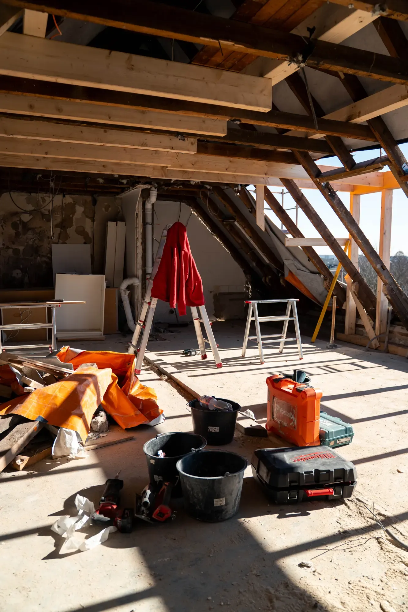 Dachgeschoss im Rohbau mit freigelegtem Sparrendachstuhl, Leiter und Werkzeugkoffern