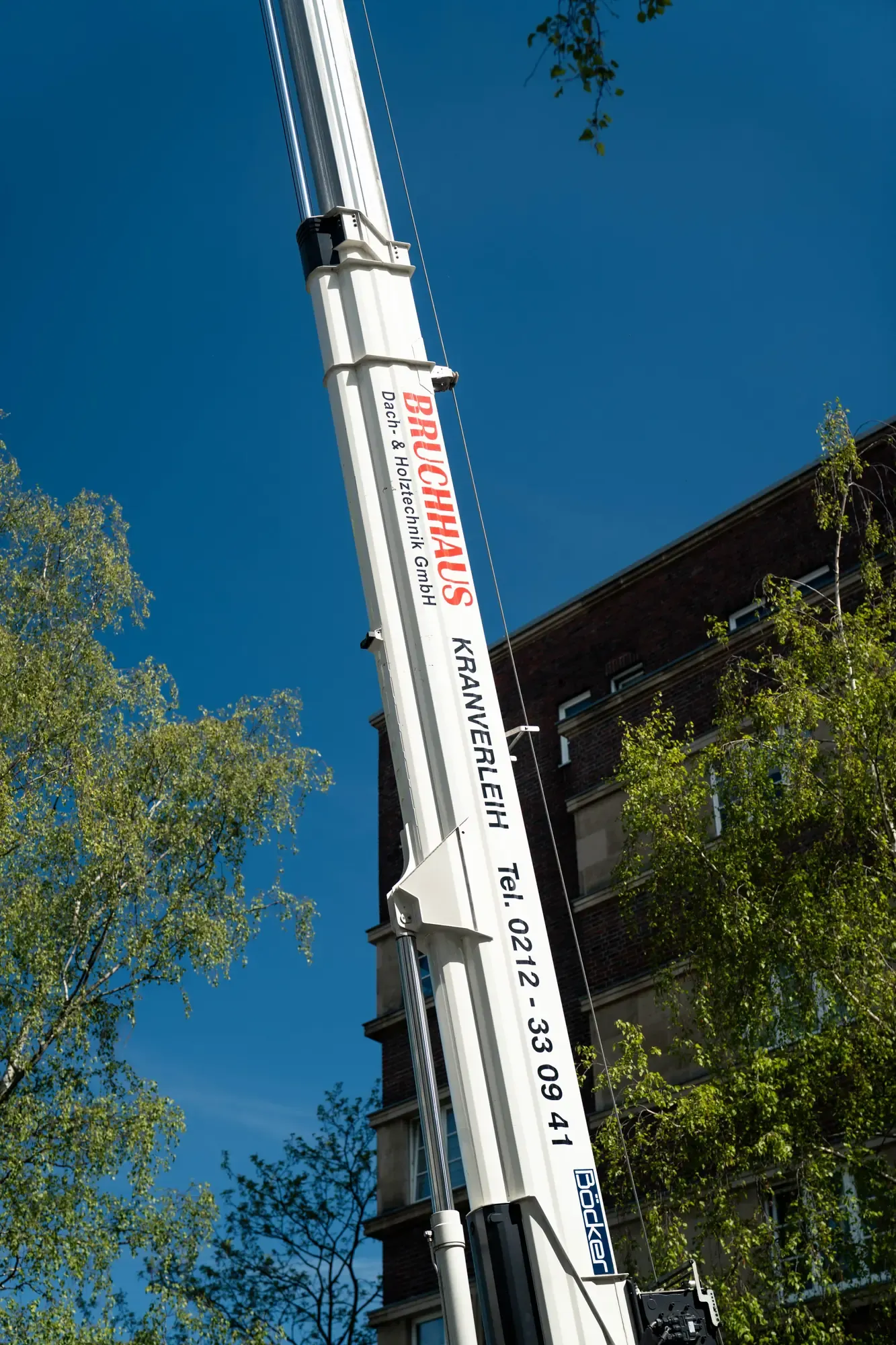 Ausgefahrener Bruchhaus-Kranarm mit Firmen-Schriftzug und Telefonnummer vor blauem Himmel